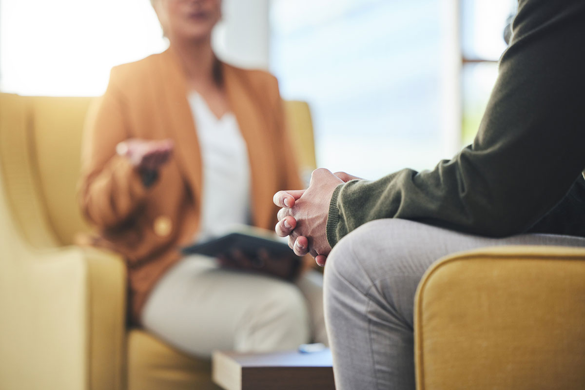 a man and a therapist sit in a room. the camera focuses on the man's clasped hands