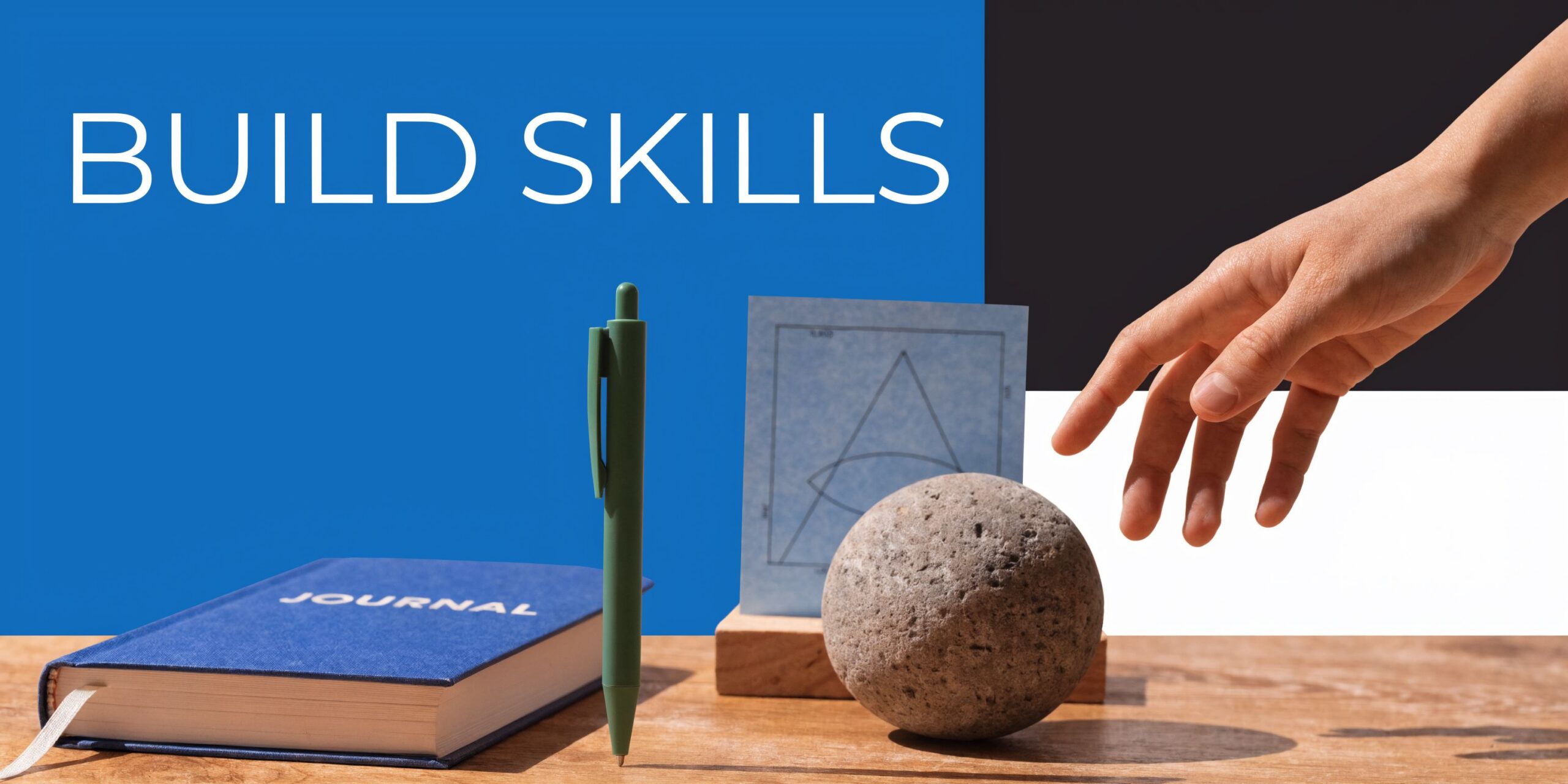 A hand reaching toward a stone, a notebook, and a geometric drawing on a wooden desk.