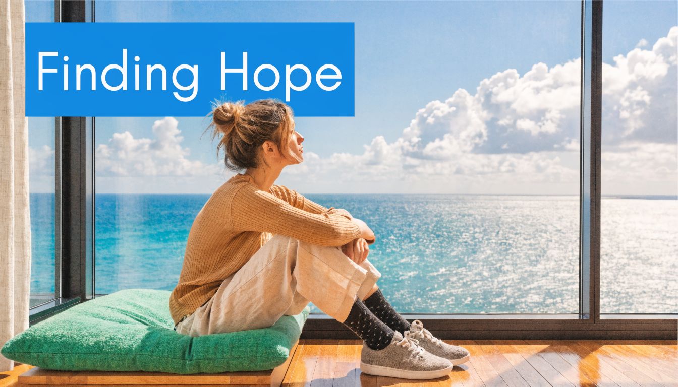 A young woman sits thoughtfully on a green floor cushion looking out at the ocean view.