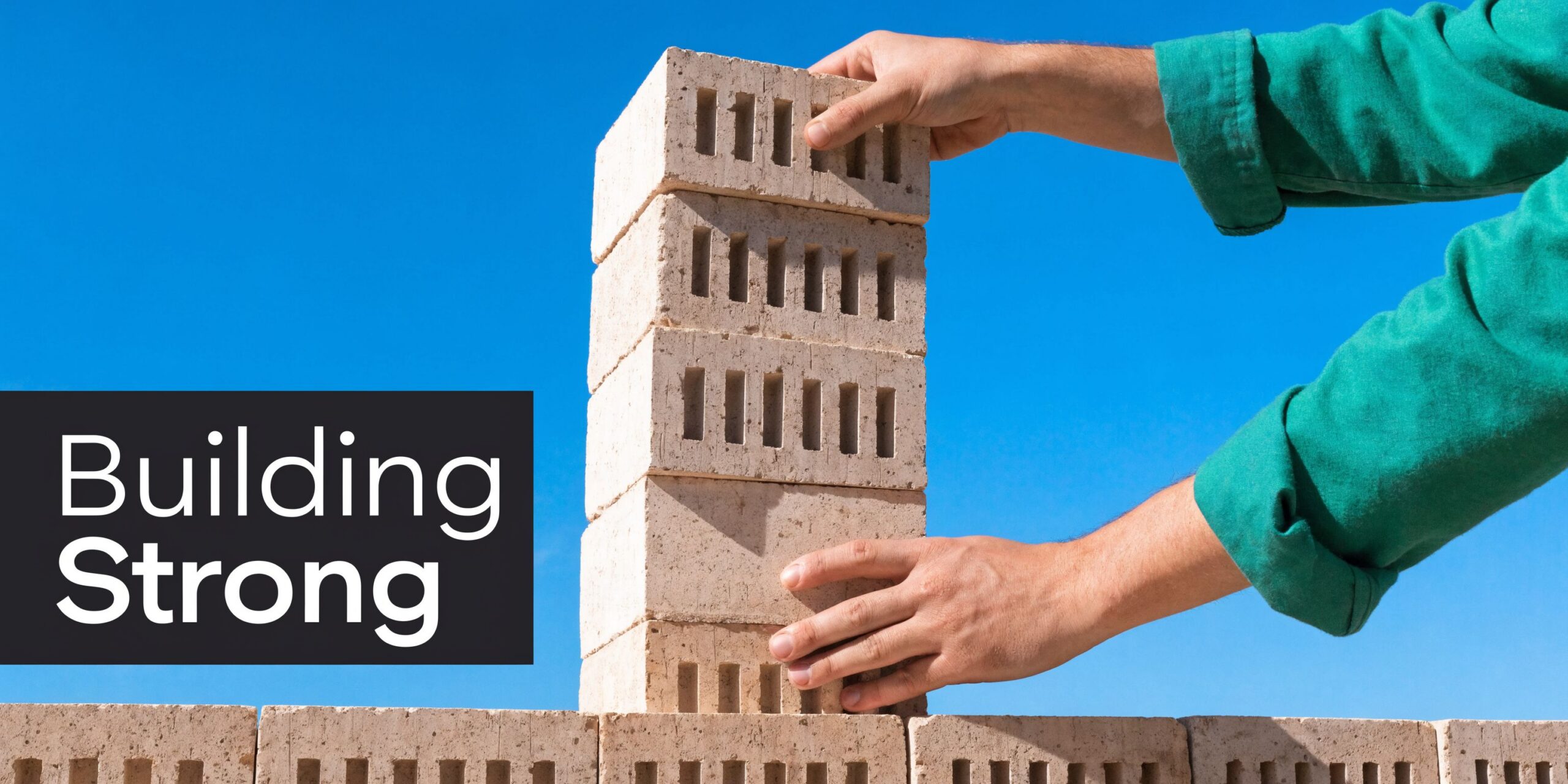 A construction worker carefully stacking light-colored bricks to build a strong wall against a blue sky.