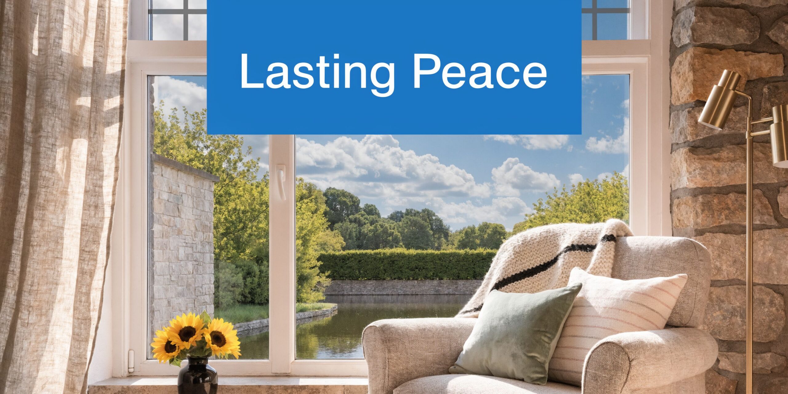 A cozy armchair with a knit blanket and pillows sits by a bright window overlooking a peaceful pond.